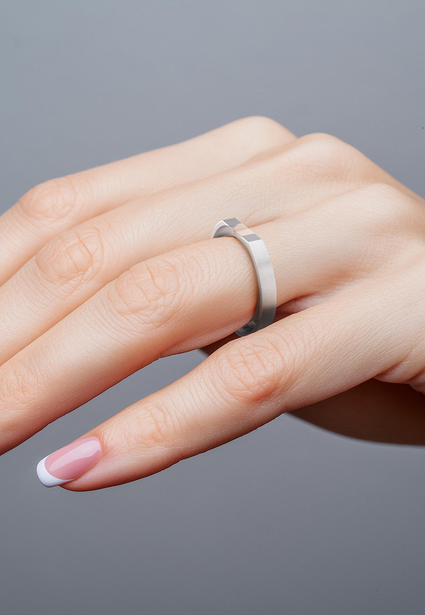 Eine Hand mit gepflegter Maniküre präsentiert den minimalistischen Taris Ring aus mattem Metall, dessen einfaches, aber elegantes Design auf dem Ringfinger zur Schau gestellt wird.